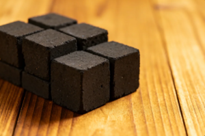 Tumpukan briket batok kelapa murni berbentuk kubus yang hitam pekat, padat, dan terlihat sangat berkualitas tinggi.