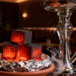 Tumpukan arang briket shisha berbentuk kubus dari tempurung kelapa yang membara merah di atas tungku shisha.
